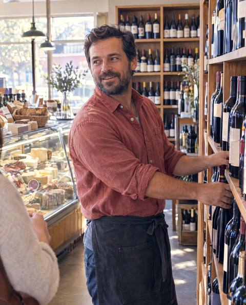 A worker restocks the shelves of a wine and deli shop.
